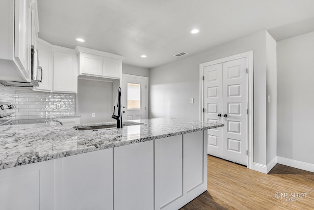 kitchen with sink, range, white cabinetry, light hardwood / wood-style floors, and light stone counters