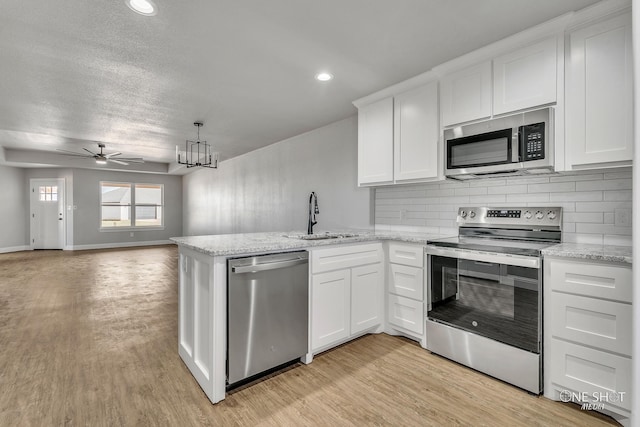 kitchen with stainless steel appliances, sink, ceiling fan with notable chandelier, and white cabinets