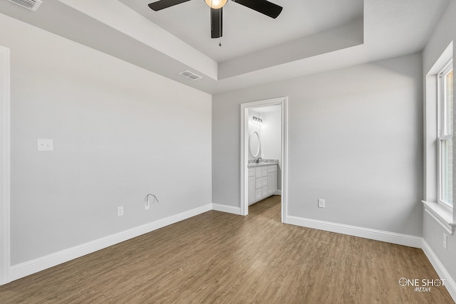 unfurnished bedroom featuring ensuite bathroom, hardwood / wood-style flooring, a tray ceiling, and ceiling fan