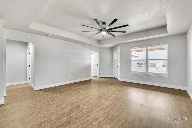 empty room with a textured ceiling, a tray ceiling, light wood-type flooring, and ceiling fan