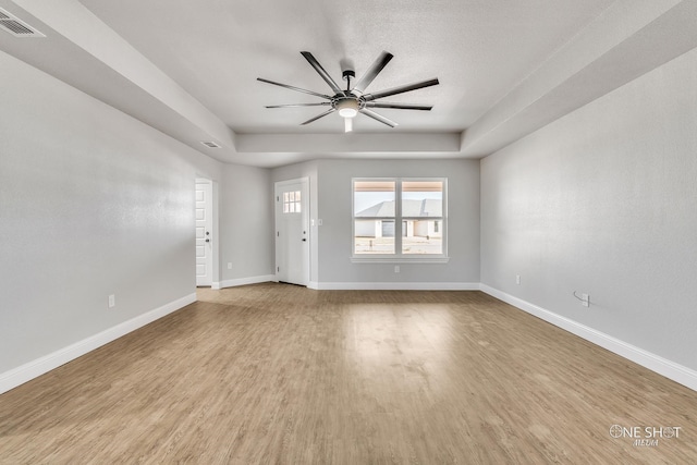 empty room featuring ceiling fan, a tray ceiling, and light hardwood / wood-style flooring