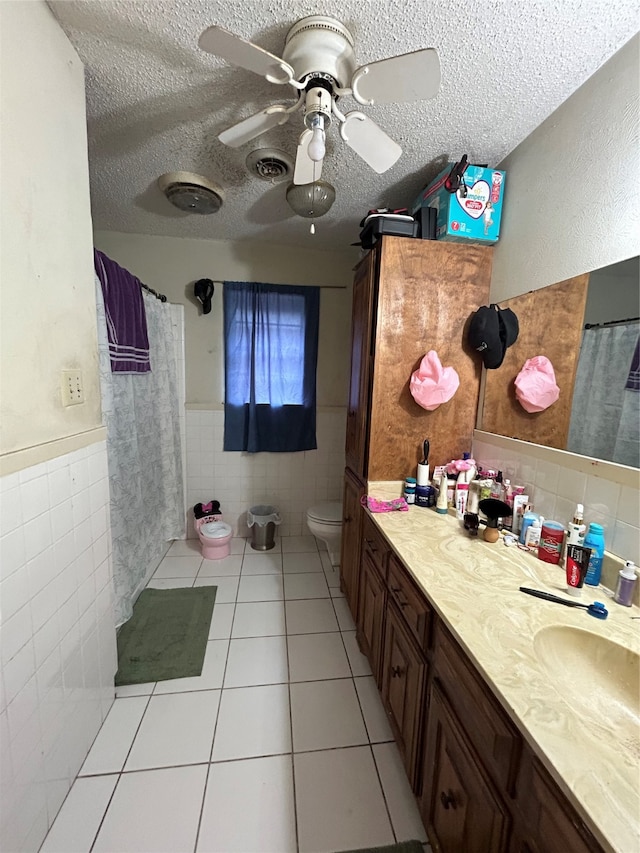 bathroom with toilet, vanity, a textured ceiling, ceiling fan, and tile walls