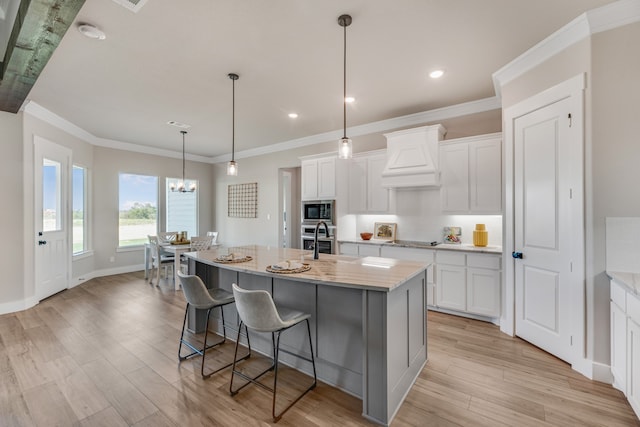 kitchen featuring white cabinets, appliances with stainless steel finishes, a center island with sink, and light hardwood / wood-style floors