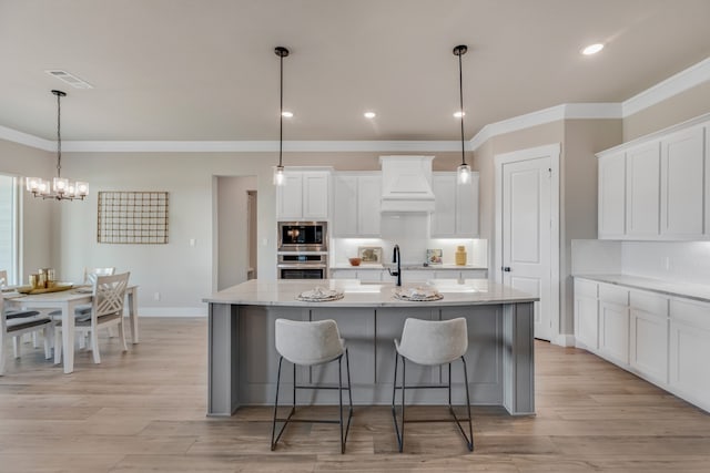 kitchen featuring white cabinets, a center island with sink, appliances with stainless steel finishes, and custom range hood