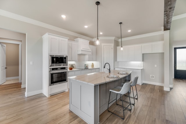 kitchen with light stone counters, white cabinets, a kitchen island with sink, stainless steel appliances, and custom range hood