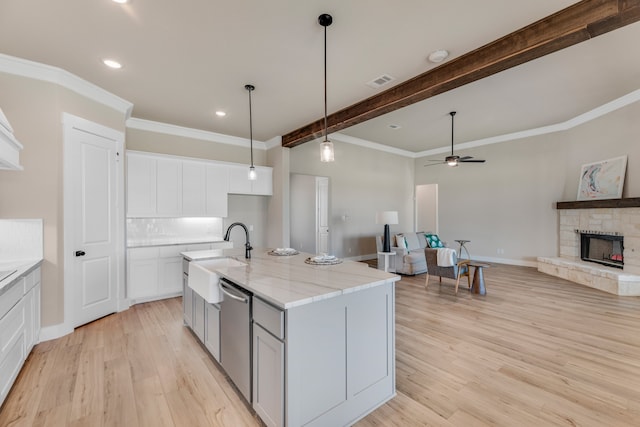 kitchen with light wood-type flooring, sink, a center island with sink, a stone fireplace, and ceiling fan