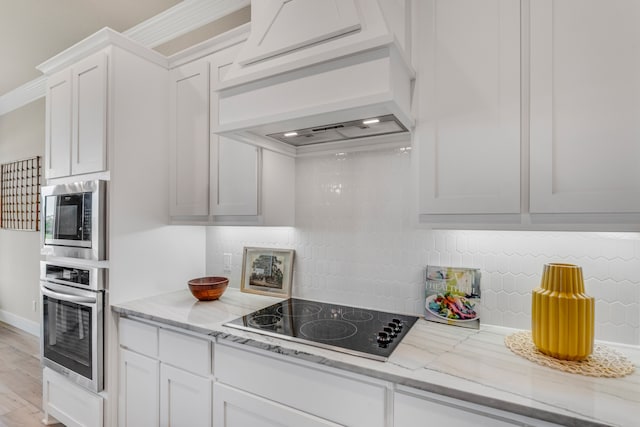 kitchen featuring custom exhaust hood, white cabinetry, appliances with stainless steel finishes, light stone countertops, and crown molding