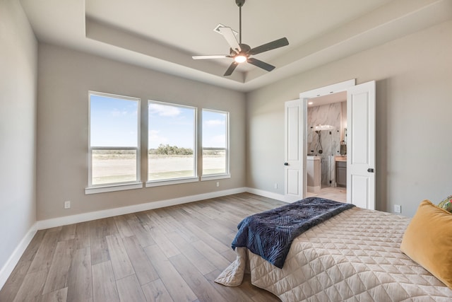 bedroom with ceiling fan, light hardwood / wood-style flooring, and a tray ceiling