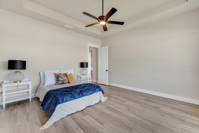 bedroom featuring light wood-type flooring, a tray ceiling, and ceiling fan