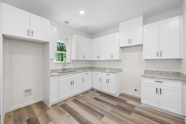 kitchen featuring light stone counters, light hardwood / wood-style floors, sink, and white cabinetry