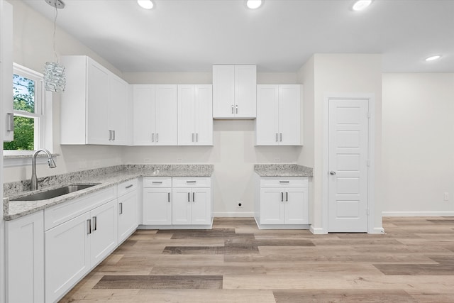 kitchen featuring pendant lighting, light wood-type flooring, sink, and white cabinetry