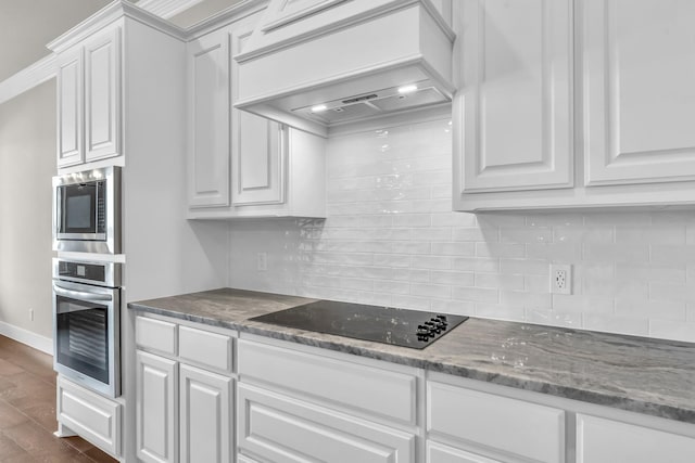 kitchen with dark wood-type flooring, custom range hood, appliances with stainless steel finishes, tasteful backsplash, and white cabinetry