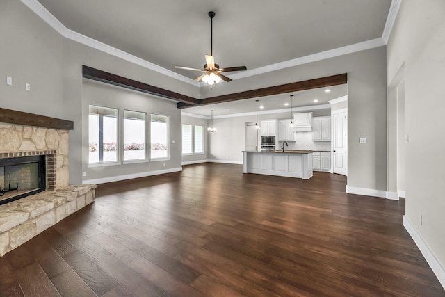 unfurnished living room with ceiling fan, sink, a stone fireplace, dark hardwood / wood-style flooring, and ornamental molding