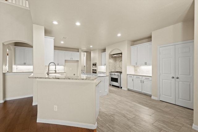 kitchen featuring light stone countertops, white cabinetry, sink, stainless steel appliances, and a center island with sink