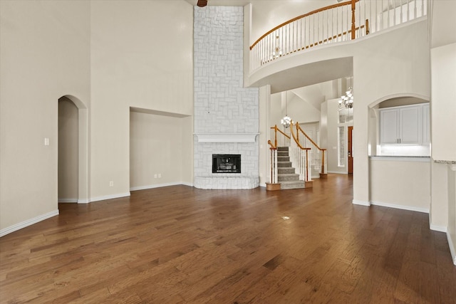 unfurnished living room featuring a stone fireplace, dark wood-type flooring, a high ceiling, and an inviting chandelier