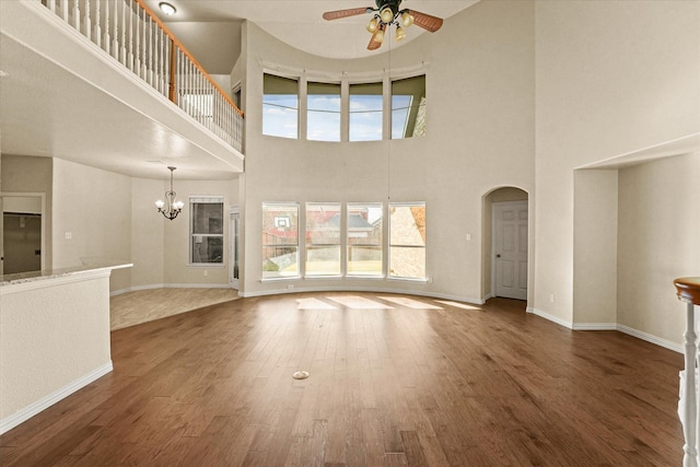 unfurnished living room with dark hardwood / wood-style flooring, plenty of natural light, ceiling fan with notable chandelier, and a high ceiling