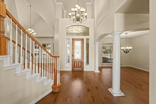 entrance foyer featuring decorative columns, dark hardwood / wood-style flooring, a towering ceiling, and an inviting chandelier