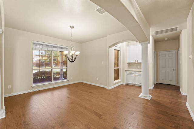 unfurnished living room with ornate columns, light hardwood / wood-style floors, and an inviting chandelier