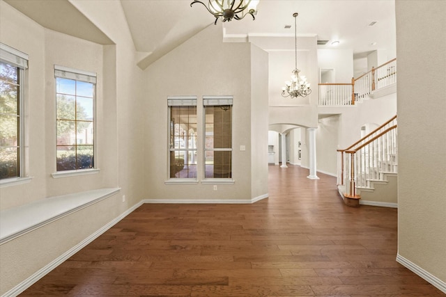 foyer entrance with decorative columns, high vaulted ceiling, dark wood-type flooring, and a notable chandelier