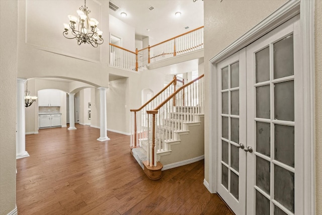 foyer with a high ceiling, french doors, hardwood / wood-style flooring, a notable chandelier, and decorative columns