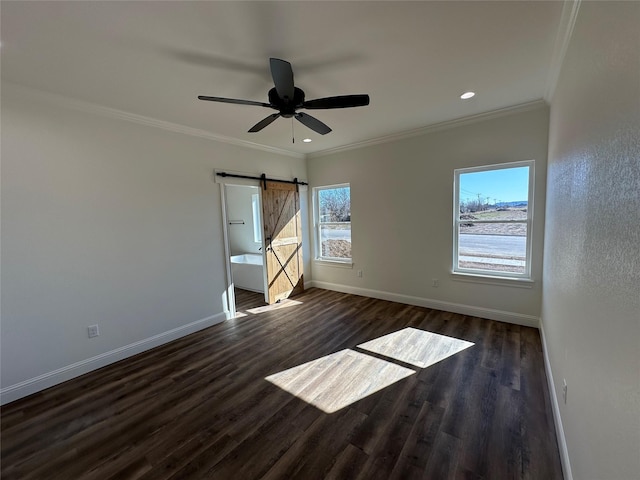 empty room with a barn door, dark wood-type flooring, a wealth of natural light, and ornamental molding