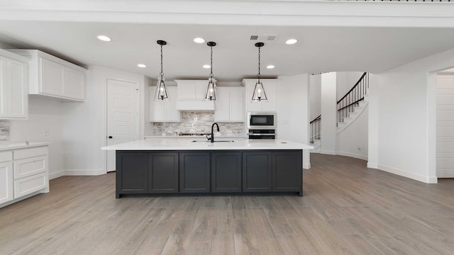 kitchen with hanging light fixtures, an island with sink, black microwave, and white cabinets