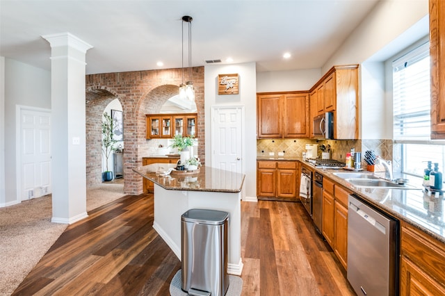 kitchen with dark wood-type flooring, tasteful backsplash, hanging light fixtures, a kitchen island, and appliances with stainless steel finishes