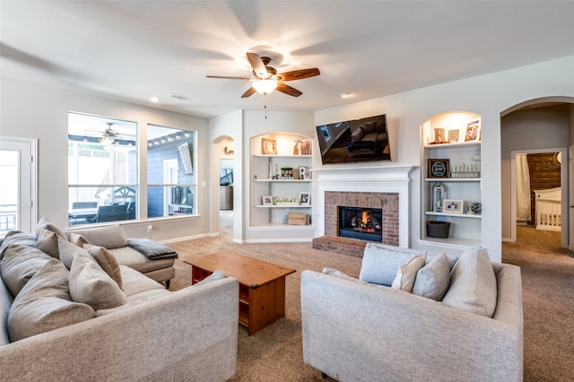 carpeted living room with a fireplace, ceiling fan, and built in shelves