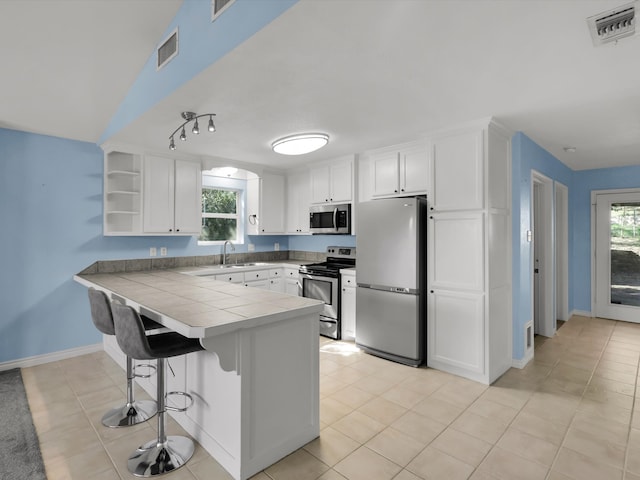 kitchen featuring a breakfast bar, kitchen peninsula, appliances with stainless steel finishes, light tile patterned flooring, and white cabinetry