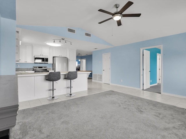 kitchen featuring kitchen peninsula, vaulted ceiling, appliances with stainless steel finishes, a kitchen bar, and white cabinetry