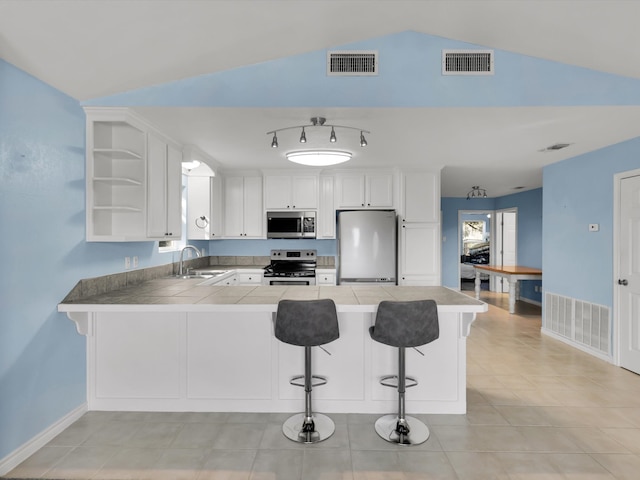 kitchen with kitchen peninsula, stainless steel appliances, vaulted ceiling, sink, and white cabinets