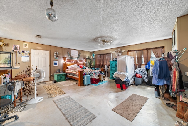 bedroom featuring a textured ceiling, concrete floors, wood walls, and ceiling fan