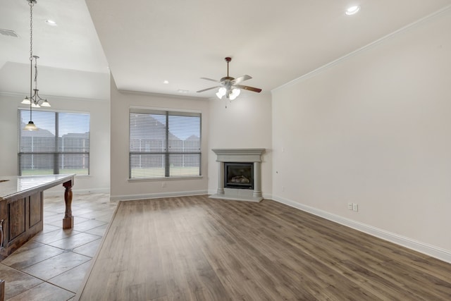 unfurnished living room with ceiling fan with notable chandelier, wood-type flooring, and ornamental molding