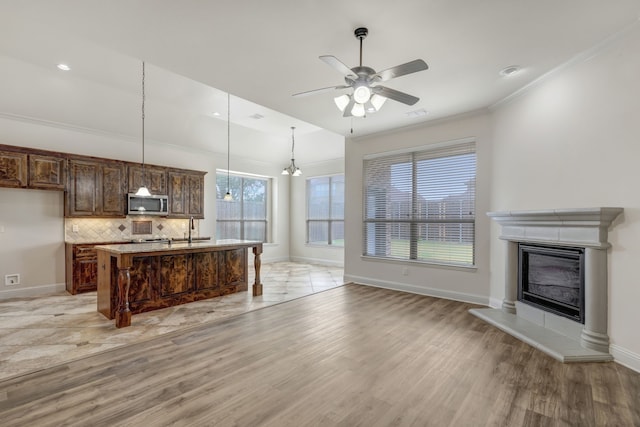 kitchen with light hardwood / wood-style flooring, decorative light fixtures, ceiling fan with notable chandelier, an island with sink, and a kitchen breakfast bar