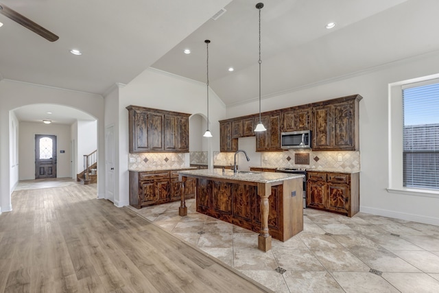 kitchen with appliances with stainless steel finishes, light hardwood / wood-style flooring, a center island with sink, and decorative backsplash