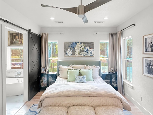 bedroom featuring a barn door, light hardwood / wood-style floors, ceiling fan, and multiple windows