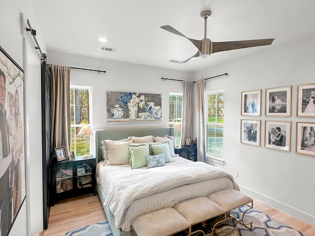 bedroom featuring ceiling fan, light hardwood / wood-style floors, and a barn door