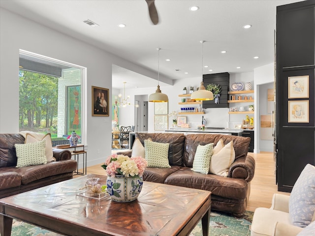 living room featuring ceiling fan with notable chandelier and light wood-type flooring