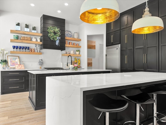 interior space with stainless steel built in refrigerator, light wood-type flooring, a kitchen island, a kitchen breakfast bar, and light stone countertops