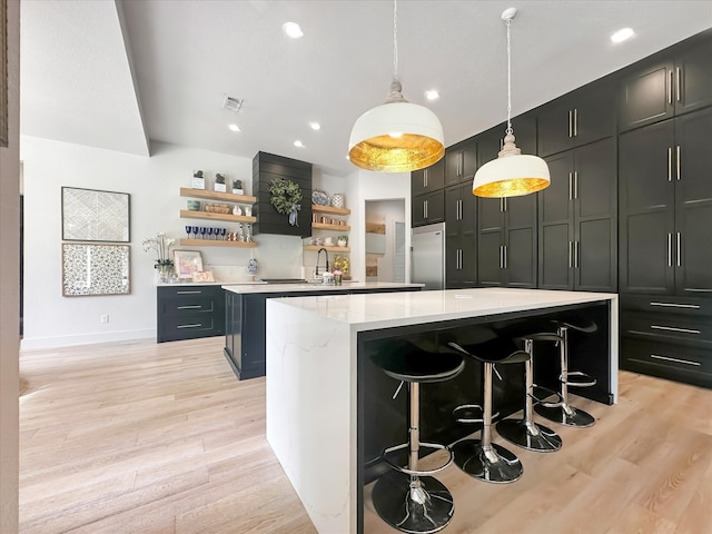 kitchen featuring light hardwood / wood-style floors, a center island, a kitchen bar, built in fridge, and decorative light fixtures