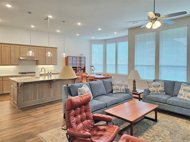 living room with ceiling fan, light wood-type flooring, and sink