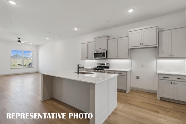 kitchen featuring a kitchen island with sink, sink, light hardwood / wood-style flooring, and appliances with stainless steel finishes