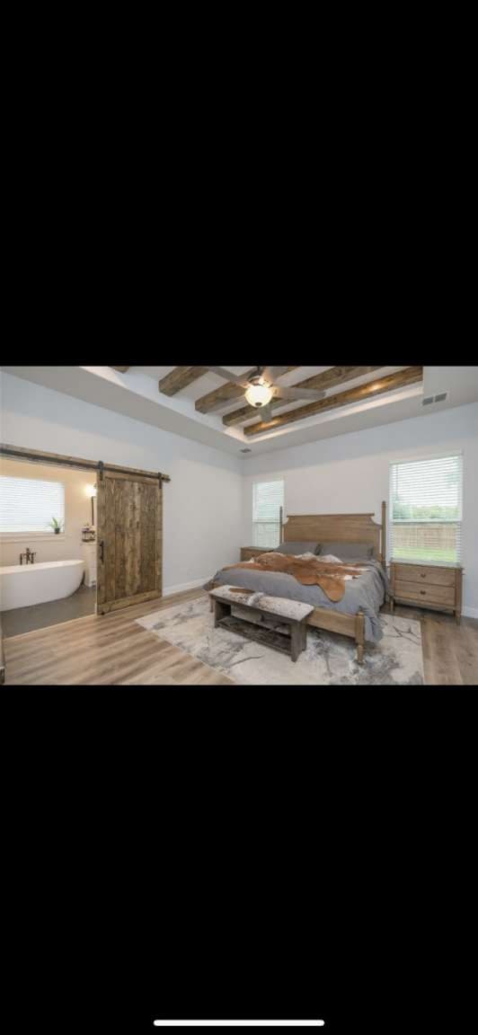 interior space with ceiling fan, wood-type flooring, beam ceiling, and a barn door