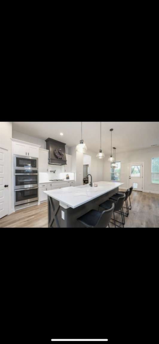 kitchen featuring hanging light fixtures, light wood-type flooring, white cabinetry, a breakfast bar area, and a center island with sink