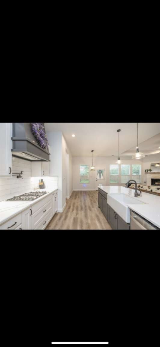 kitchen with decorative light fixtures, white cabinets, stainless steel gas stovetop, and light hardwood / wood-style floors