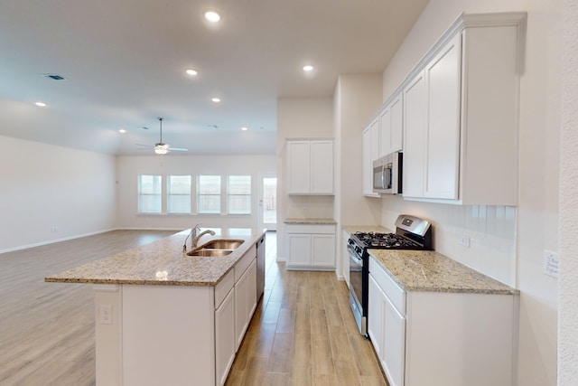 kitchen with appliances with stainless steel finishes, an island with sink, light stone countertops, sink, and white cabinetry