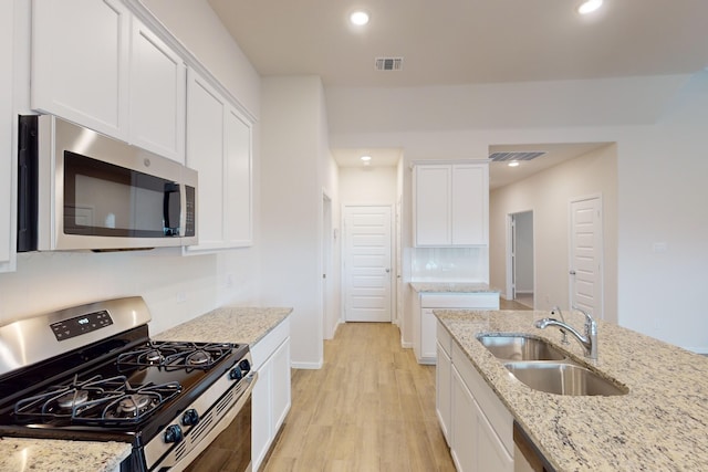 kitchen featuring light stone countertops, stainless steel appliances, light wood-type flooring, white cabinetry, and sink