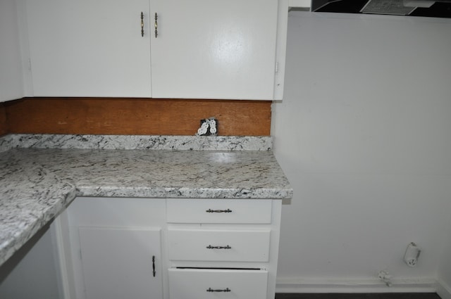 kitchen with exhaust hood, light stone countertops, and white cabinets