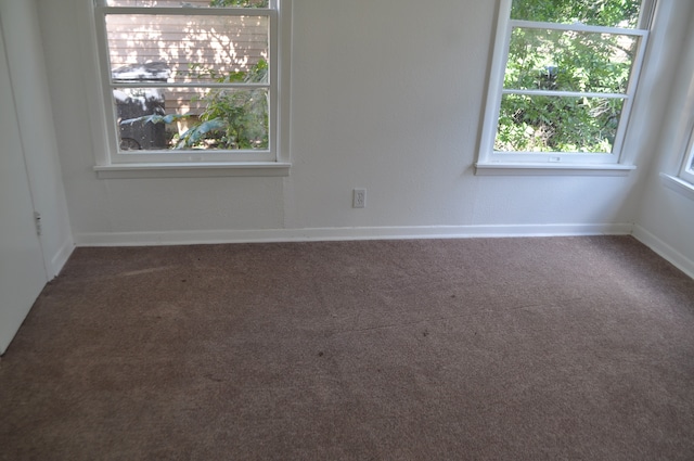 unfurnished room featuring dark colored carpet and a healthy amount of sunlight