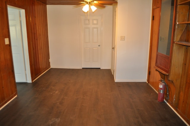 empty room featuring dark hardwood / wood-style flooring, ceiling fan, and wooden walls